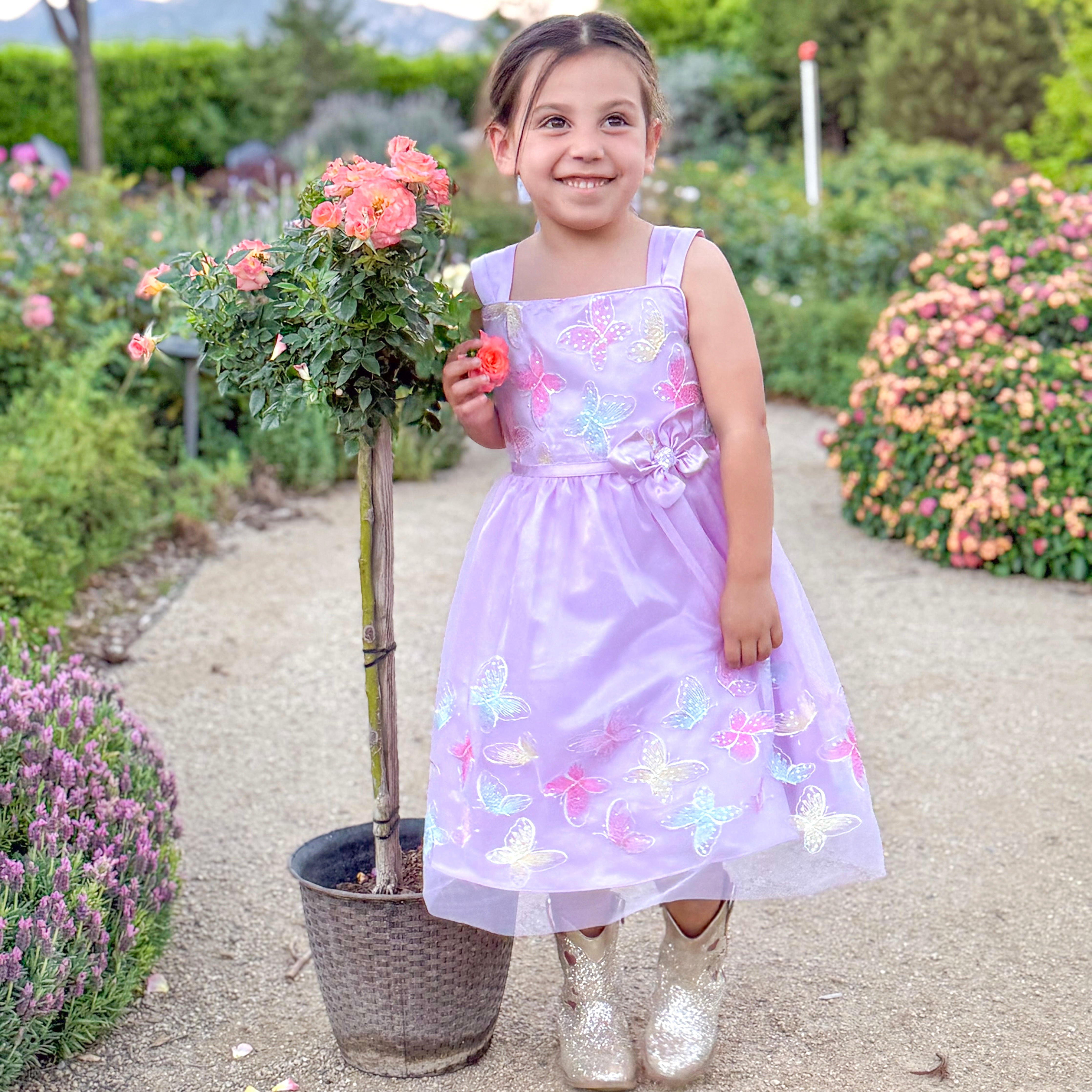 Young girl in a purple dress with butterfly patterns standing in a garden.