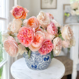 Vase of pink and peach flowers on a marble table with a blurred indoor background